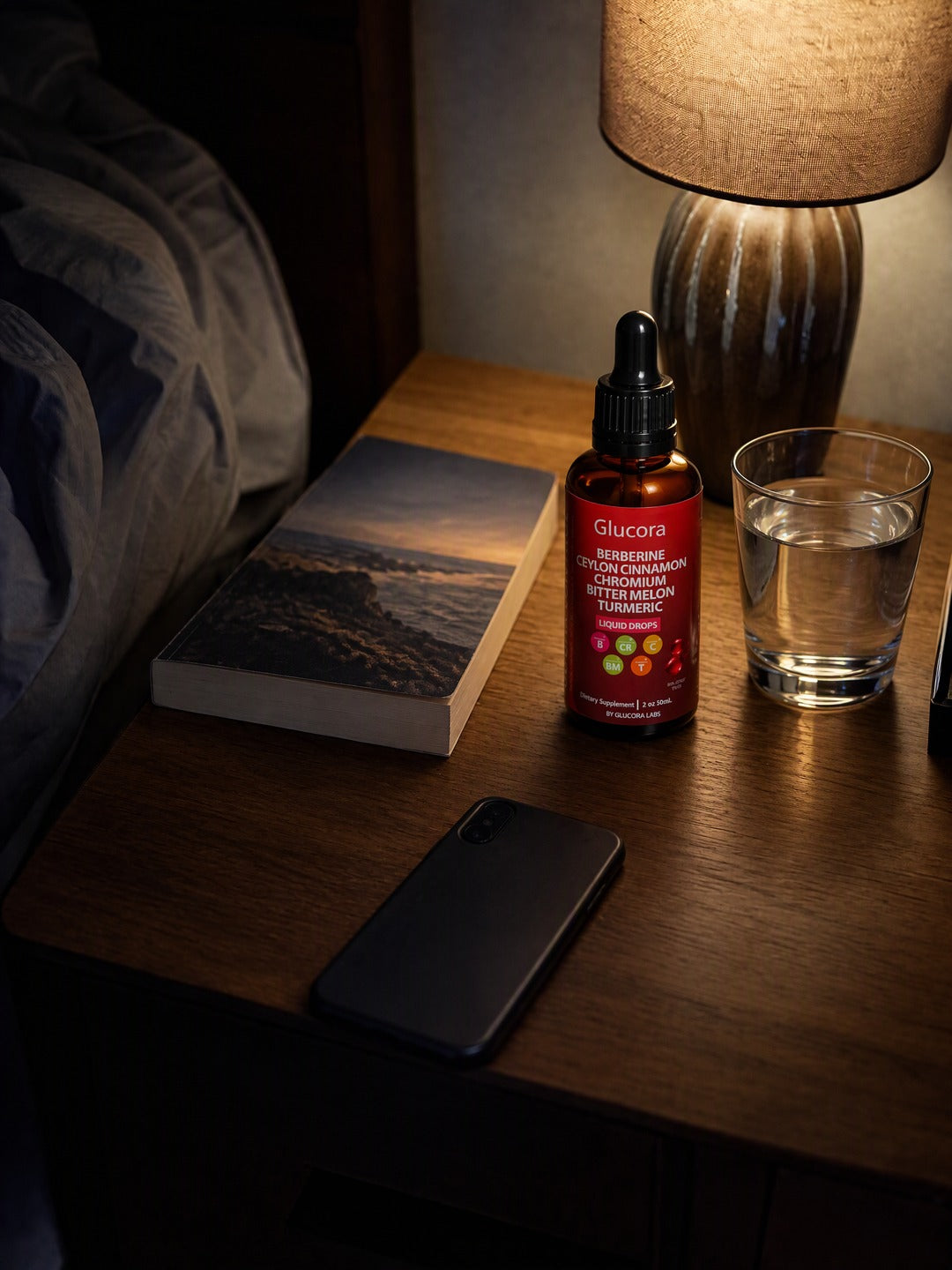 La misma mesa de noche con un vaso de agua, el frasco de Glucora y un libro