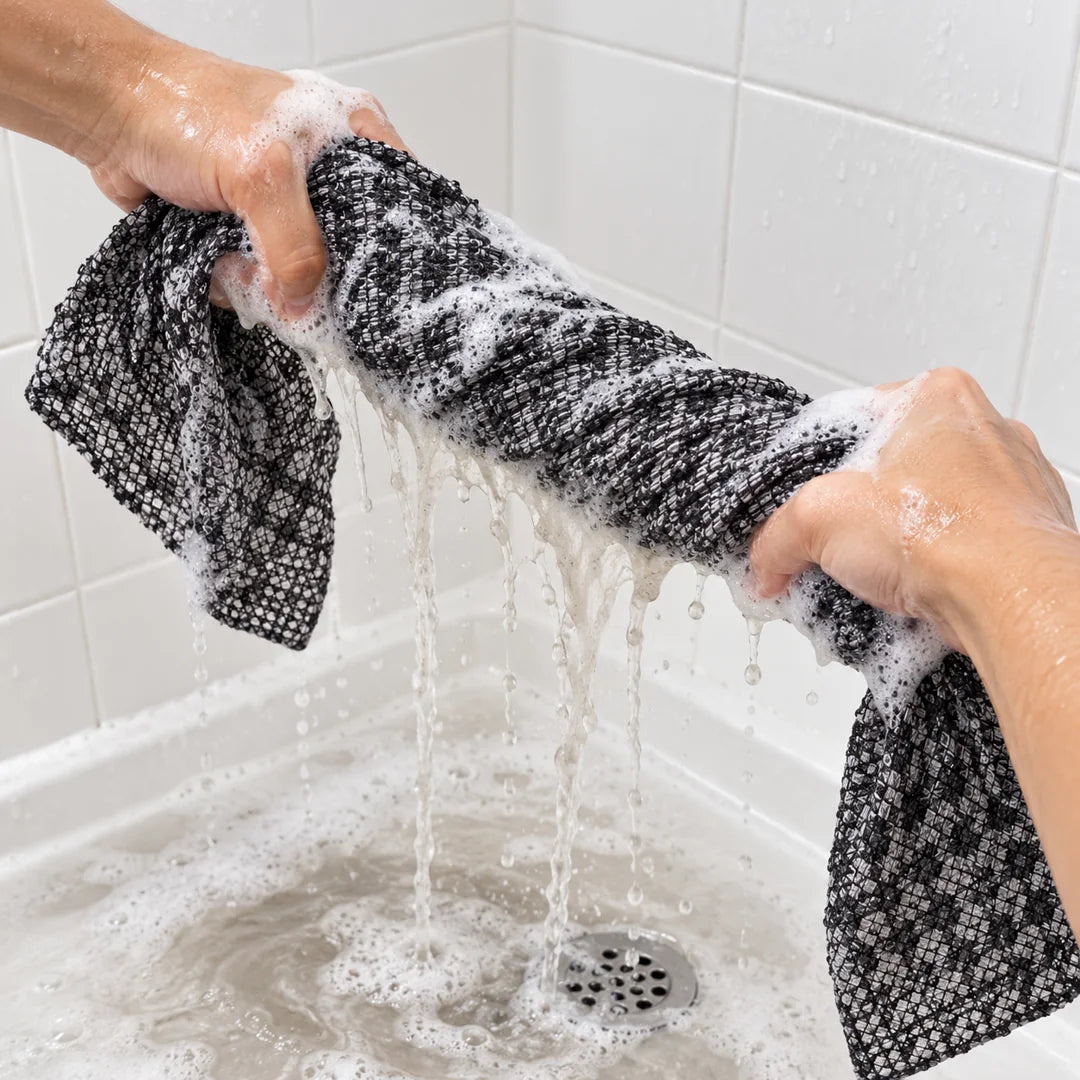 Manos escurriendo la toalla exfoliante con espuma en la ducha